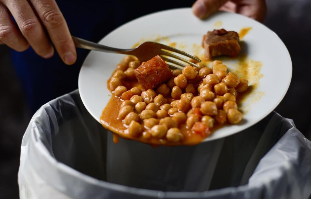 closeup of a young man throwing the leftover of a plate of chickpea stew to the trash bin