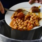 closeup of a young man throwing the leftover of a plate of chickpea stew to the trash bin