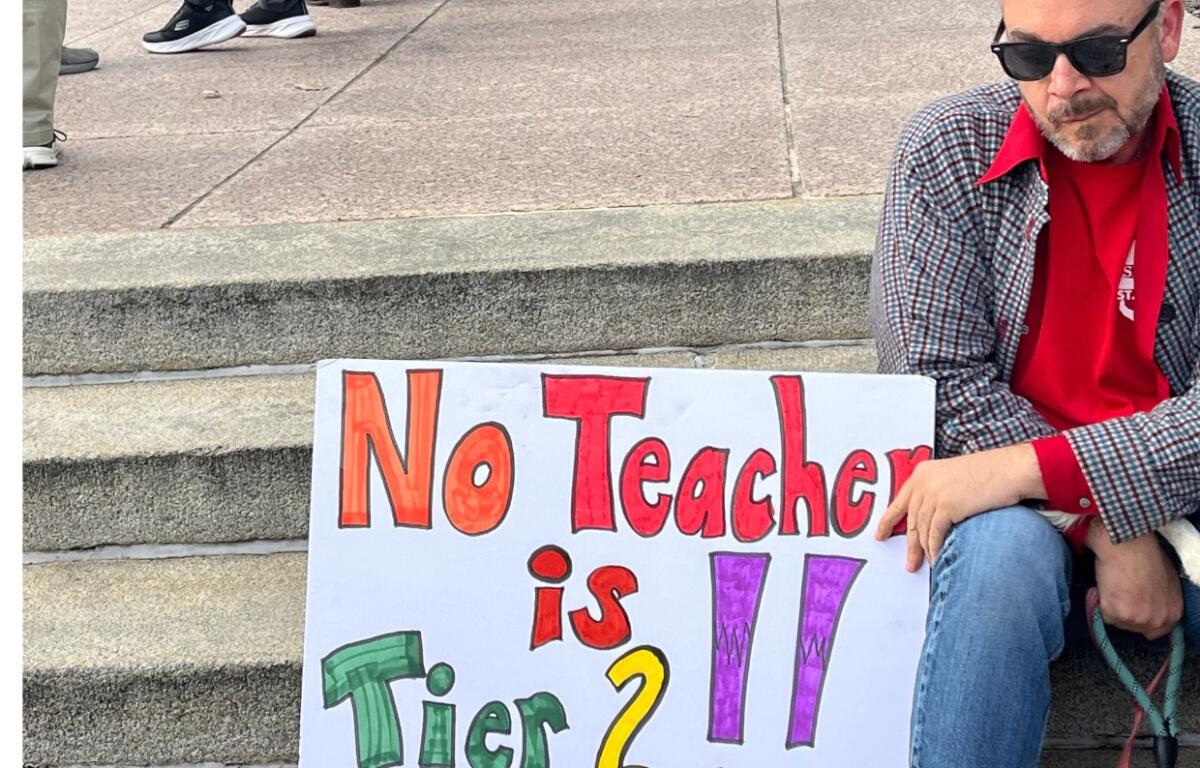 Protestor at rally holds sign saying "No Teacher is Tier 2"