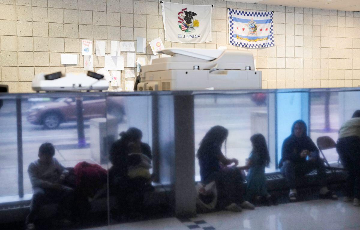 Immigrants from Venezuela are reflected in a marble wall while taking shelter at the Chicago Police Department's 16th District station on May 1, 2023. (AP Photo/Charles Rex Arbogast, FIle)