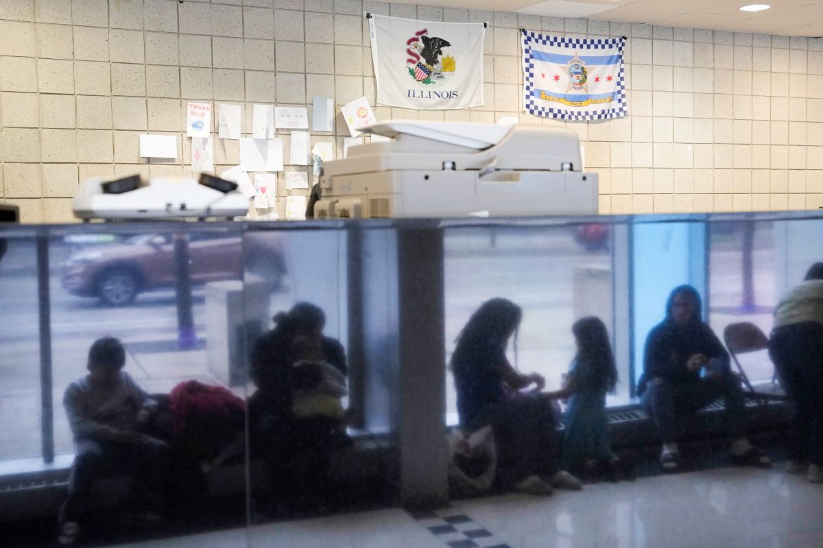 Immigrants from Venezuela are reflected in a marble wall while taking shelter at the Chicago Police Department's 16th District station on May 1, 2023. (AP Photo/Charles Rex Arbogast, FIle)