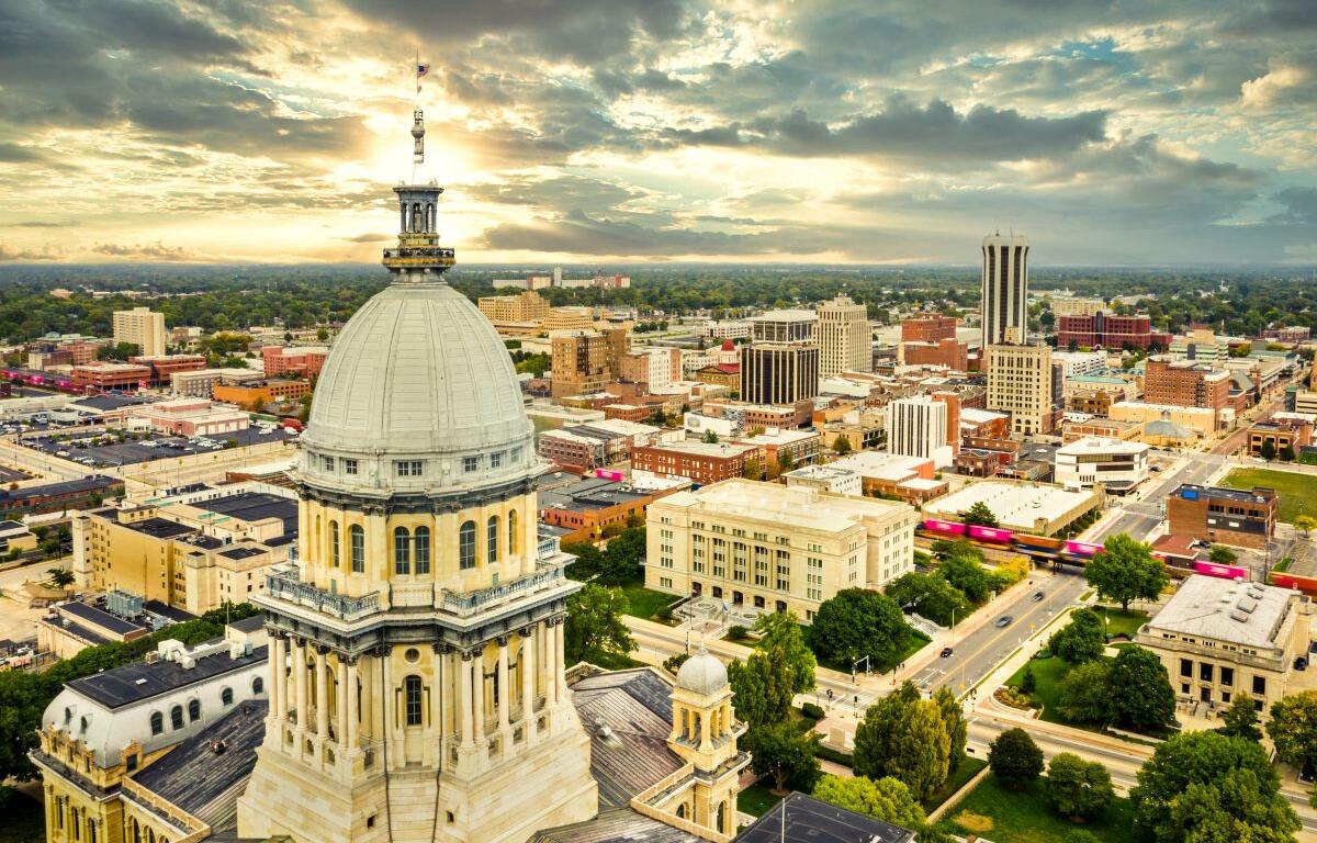 Aerial view of the Illinois State Capitol dome and Springfield skyline under a dramatic sunset