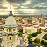 Aerial view of the Illinois State Capitol dome and Springfield skyline under a dramatic sunset