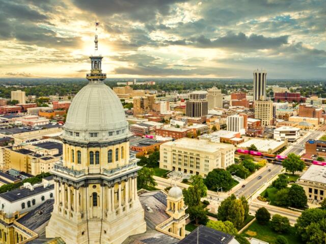 Aerial view of the Illinois State Capitol dome and Springfield skyline under a dramatic sunset