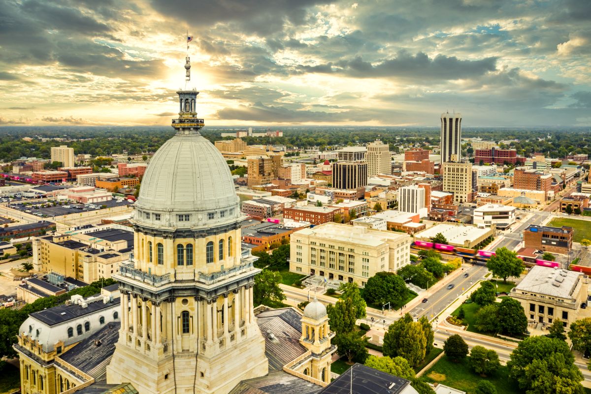 Aerial view of the Illinois State Capitol dome and Springfield skyline under a dramatic sunset
