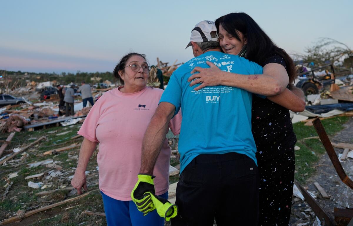 Bea Johnson, left, looks to her sister Kristie Sexton, right, as she is embraced by family friend Keith Adams as they stand next to Sexton's destroyed home after a severe storm passed through the area, Saturday, May 17, 2025, in London, Ky. (AP Photo/Carolyn Kaster)