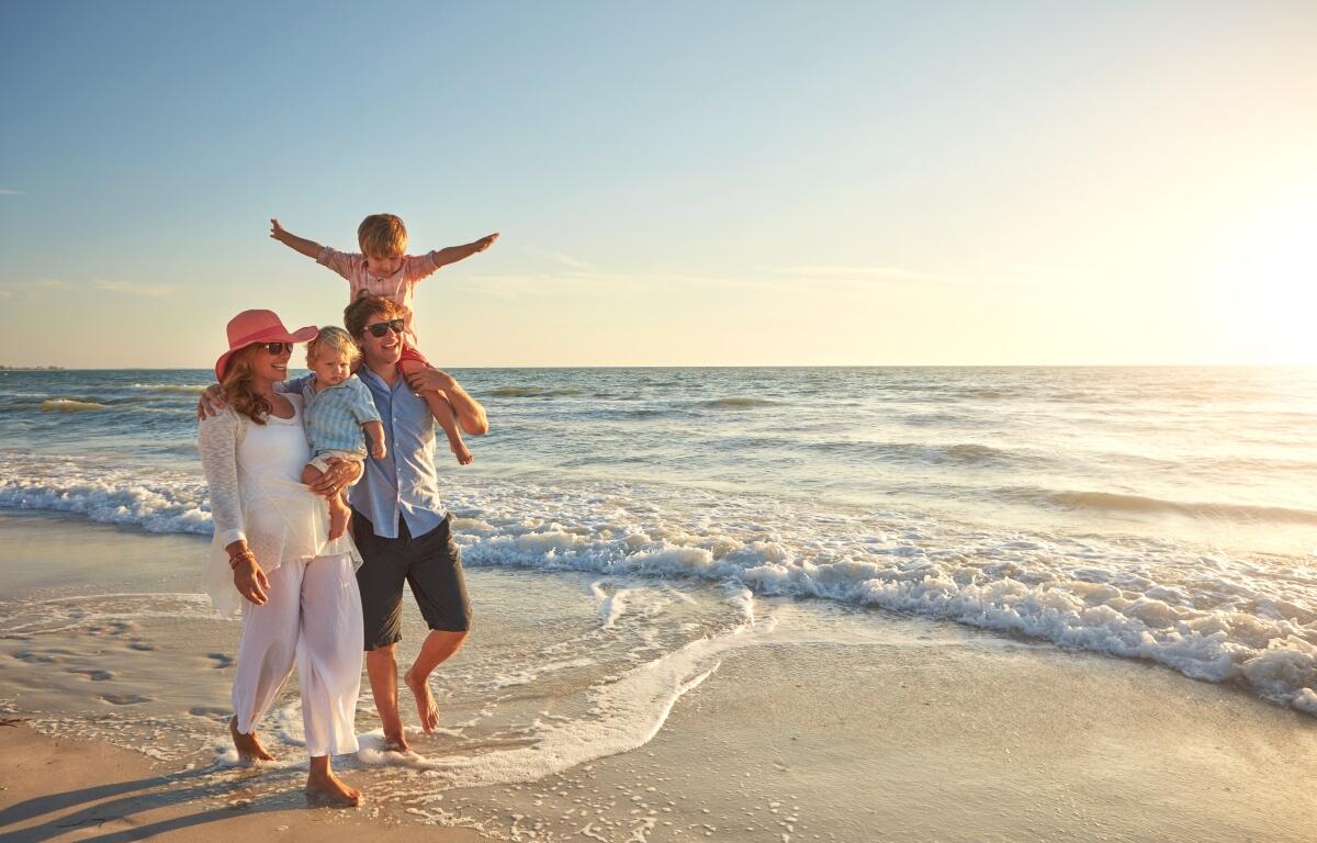 A family walking down the beach with the sun out.