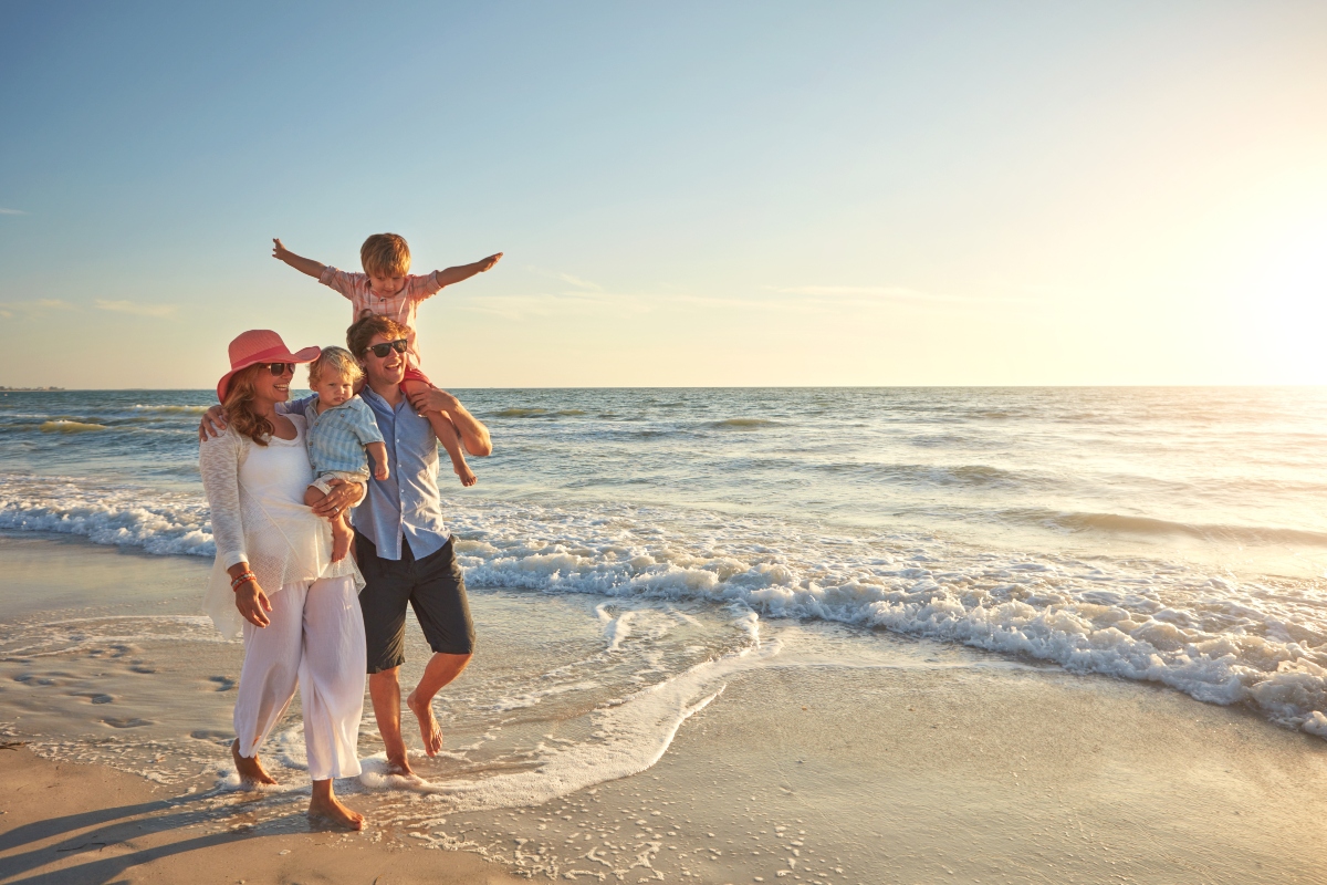 A family walking down the beach with the sun out.