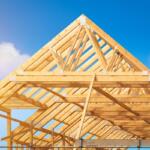 Building construction of house - Timber framing stage of a new residential home attic construction using trusses for roof structure. A construction site set against a clear blue sky.