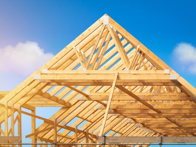 Building construction of house - Timber framing stage of a new residential home attic construction using trusses for roof structure. A construction site set against a clear blue sky.