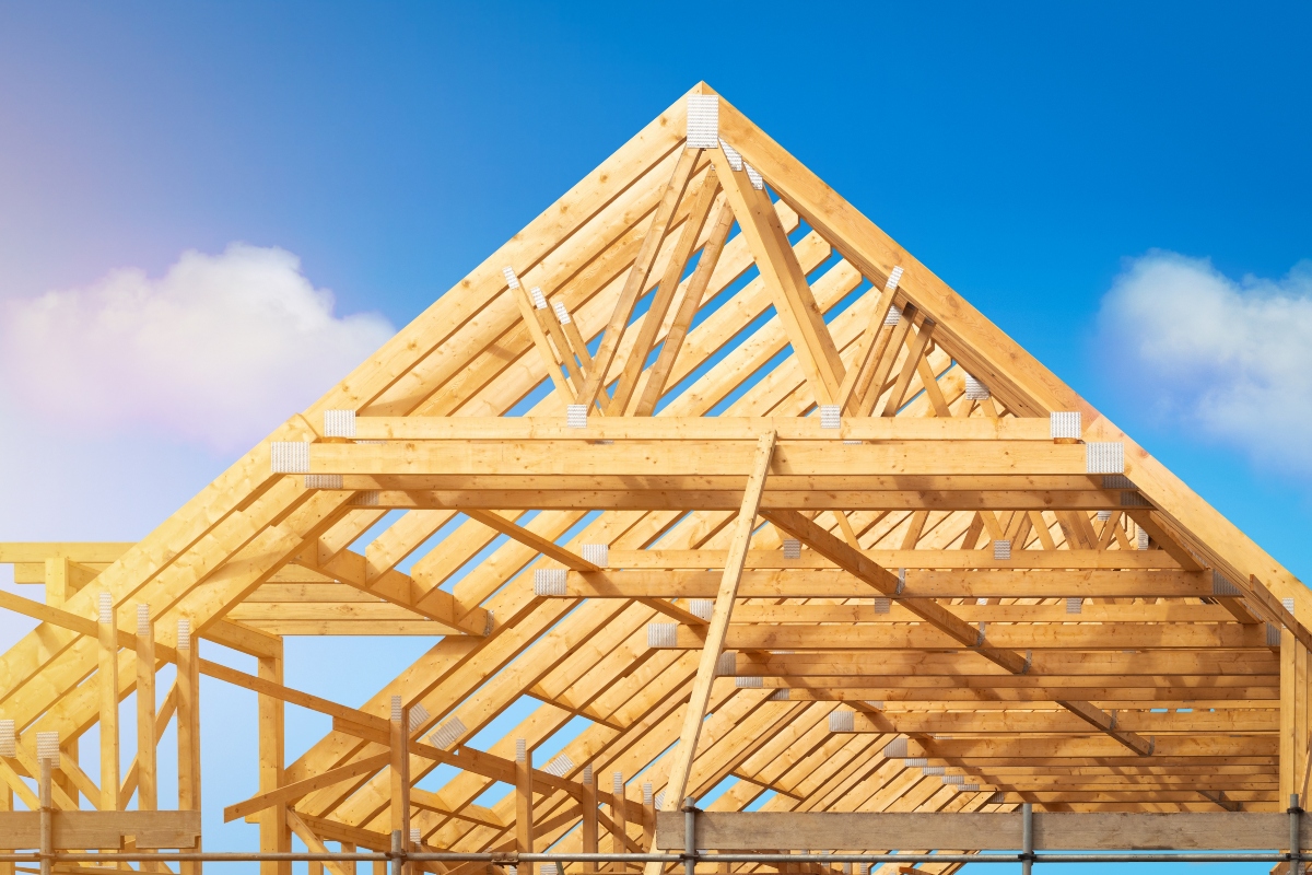 Building construction of house - Timber framing stage of a new residential home attic construction using trusses for roof structure. A construction site set against a clear blue sky.