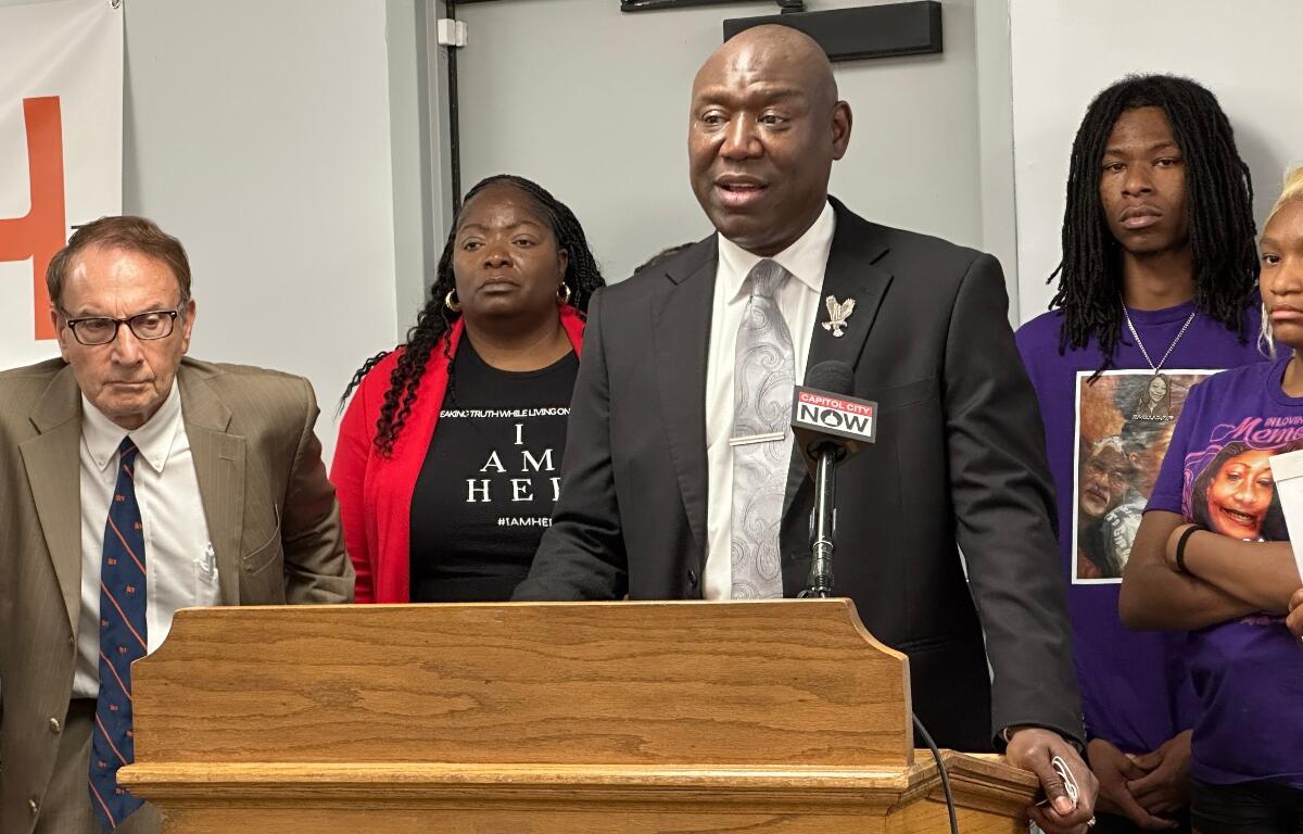 Anjanette Young, dressed in red and black, stands behind attorney Benjamin Crump during a news conference following the signing of "Sonya's Law."