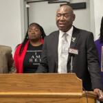 Anjanette Young, dressed in red and black, stands behind attorney Benjamin Crump during a news conference following the signing of "Sonya's Law."