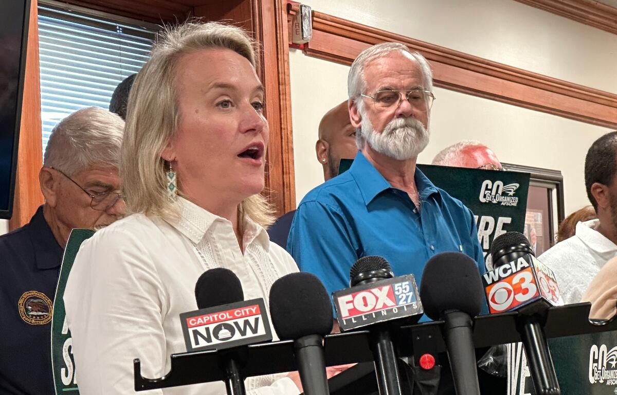 Springfield resident Bob Croteau, in blue, stands near Rep. Nikki Budzinski (D-Springfield) at a news conference at the AFL-CIO headquarters in downtown Springfield. Crouteau was one of a number of AFSCME union members who surrounded the Congresswoman.