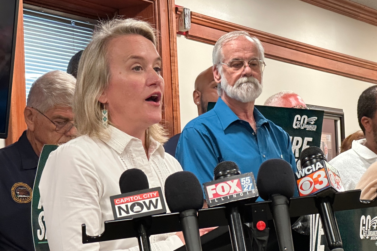 Springfield resident Bob Croteau, in blue, stands near Rep. Nikki Budzinski (D-Springfield) at a news conference at the AFL-CIO headquarters in downtown Springfield. Crouteau was one of a number of AFSCME union members who surrounded the Congresswoman.