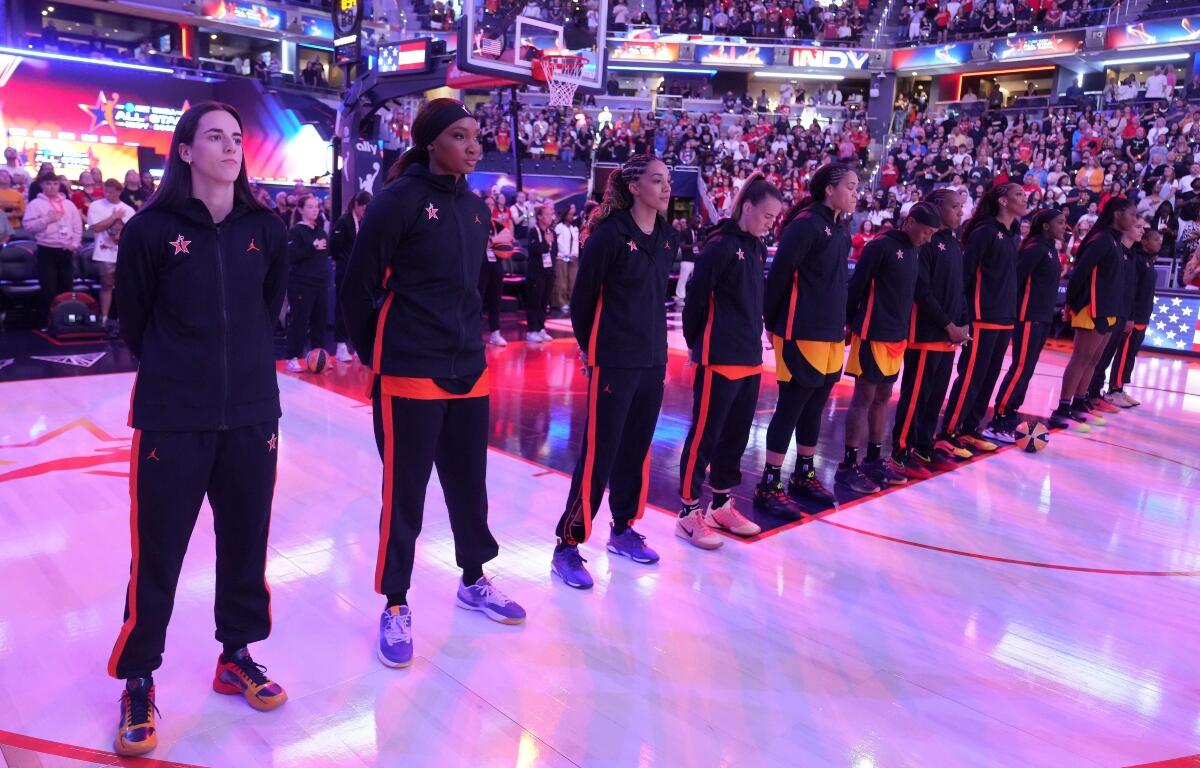 Indiana Fever's Caitlin Clark, left, stands with Team Clark during the national anthem before the WNBA All-Star basketball game, Saturday, July 19, 2025, in Indianapolis. (AP Photo/Michael Conroy)