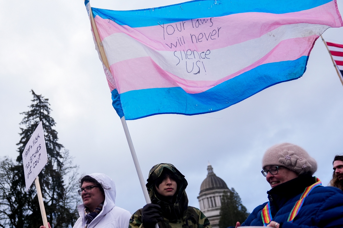 FILE - Liv Y., center, holds a transgender pride flag as people gather to protest against the Trump administration and Project 2025 near the Washington State Capitol building, in in Olympia, Wash., Feb. 5, 2025. (AP Photo/Lindsey Wasson, File)