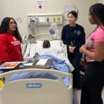 Students in the "Nurse for a Day" program hosted by UIS look over a simulated patient.