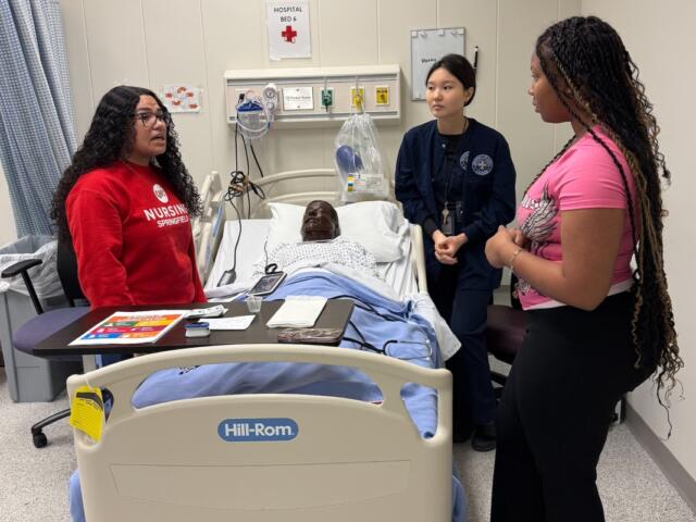 Students in the "Nurse for a Day" program hosted by UIS look over a simulated patient.
