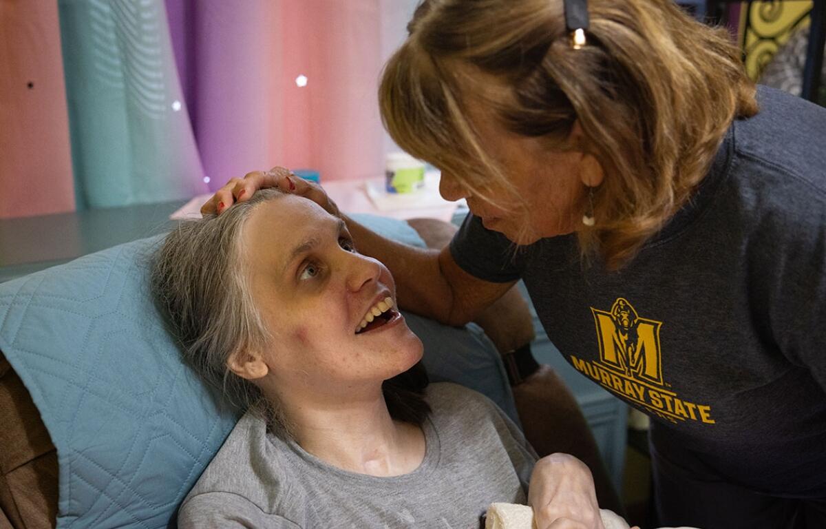 Cortnie Stewart, who suffered a traumatic brain injury in a 1997 car crash, looks up at her mother Judy Stegle at their home in Jonesboro, Illinois. A nearby nonprofit provided respite services to aid in her full-time care before closing as result of the budget impasse. (Julia Rendleman for CNI)