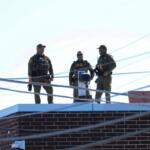 Three men in Customs and Border Protection uniforms stand on the roof of a Broadview immigration facility taking pictures of the surrounding area on Oct. 9. (Capitol News Illinois photo by Andrew Adams)