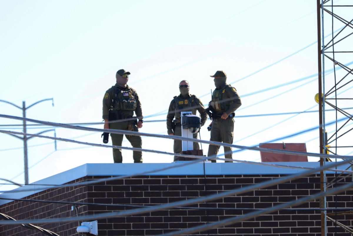 Three men in Customs and Border Protection uniforms stand on the roof of a Broadview immigration facility taking pictures of the surrounding area on Oct. 9. (Capitol News Illinois photo by Andrew Adams)