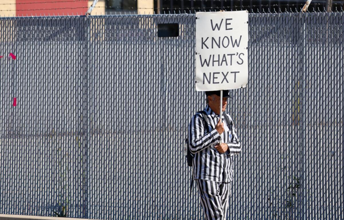 A protestor dressed in striped clothing reminiscent of uniforms worn by those imprisoned in Nazi concentration camps walks with a sign outside the U.S. Immigration and Customs Enforcement processing facility in the Chicago suburb of Broadview on Oct. 9. (Capitol News Illinois photo by Andrew Adams)