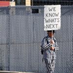 A protestor dressed in striped clothing reminiscent of uniforms worn by those imprisoned in Nazi concentration camps walks with a sign outside the U.S. Immigration and Customs Enforcement processing facility in the Chicago suburb of Broadview on Oct. 9. (Capitol News Illinois photo by Andrew Adams)