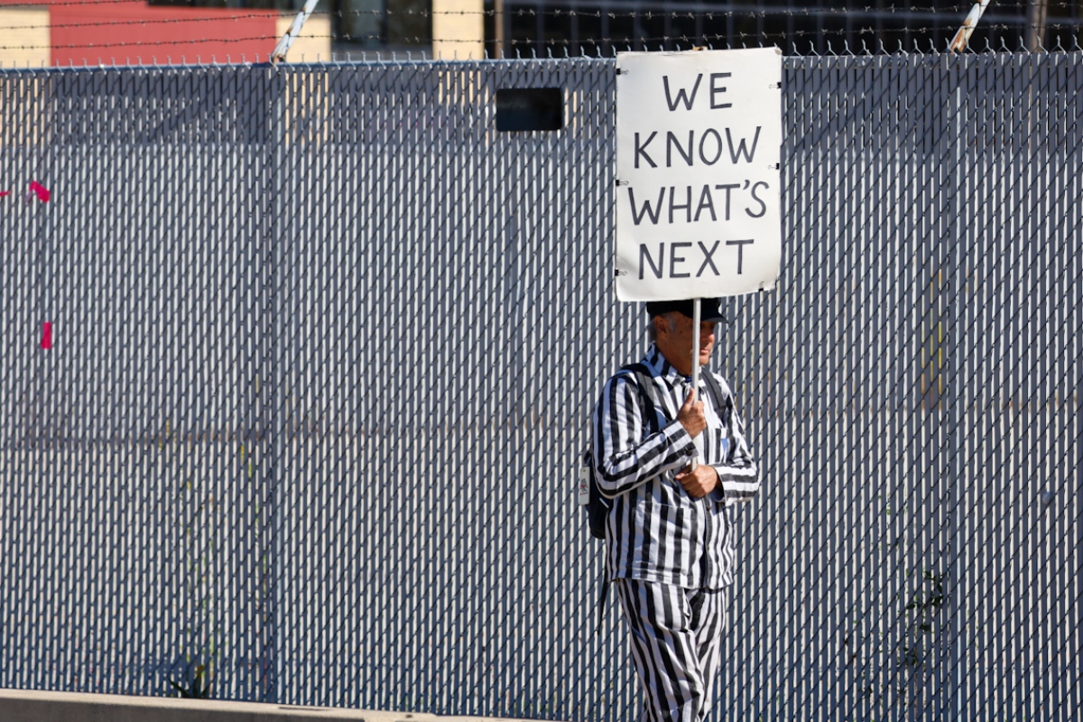 A protestor dressed in striped clothing reminiscent of uniforms worn by those imprisoned in Nazi concentration camps walks with a sign outside the U.S. Immigration and Customs Enforcement processing facility in the Chicago suburb of Broadview on Oct. 9. (Capitol News Illinois photo by Andrew Adams)