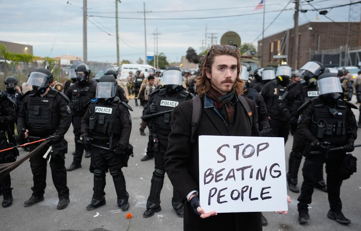 A demonstrator holds a sign reading "STOP BEATING PEOPLE" near a line of law enforcement as protesters gather outside an ICE processing facility in the Chicago suburb of Broadview, Ill., Saturday, Nov. 1, 2025. (AP Photo/Alex Brandon)
