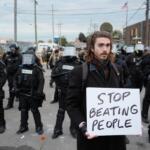 A demonstrator holds a sign reading "STOP BEATING PEOPLE" near a line of law enforcement as protesters gather outside an ICE processing facility in the Chicago suburb of Broadview, Ill., Saturday, Nov. 1, 2025. (AP Photo/Alex Brandon)