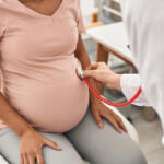 Doctor listens to a pregnant woman’s abdomen using a stethoscope.