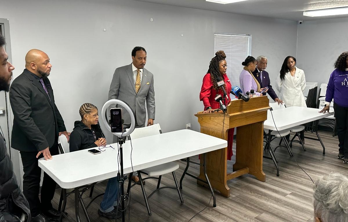 Friends, family, and supporters of Sonya Massey gather Thursday at a press conference following the sentence being read in the Sean Grayson trial. Teresa Haley, dressed in red, speaks at a podium.