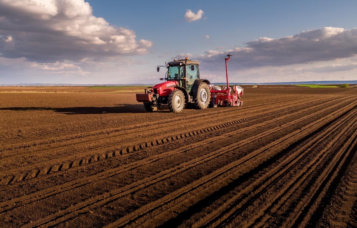 Tractor planting seeds in a cultivated agricultural field under a cloudy sky