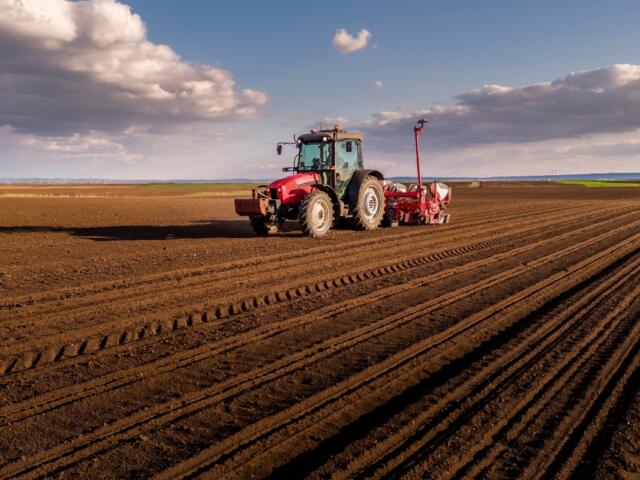 Tractor planting seeds in a cultivated agricultural field under a cloudy sky
