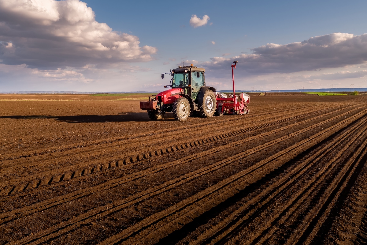 Tractor planting seeds in a cultivated agricultural field under a cloudy sky