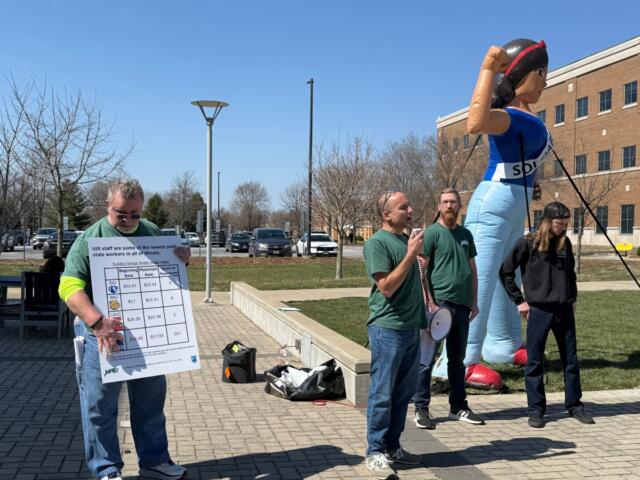 Dathan Powell (center, in green), chair of UIS United Faulty, speaks as the results of a strike authorization vote were made public Thursday, March 19.