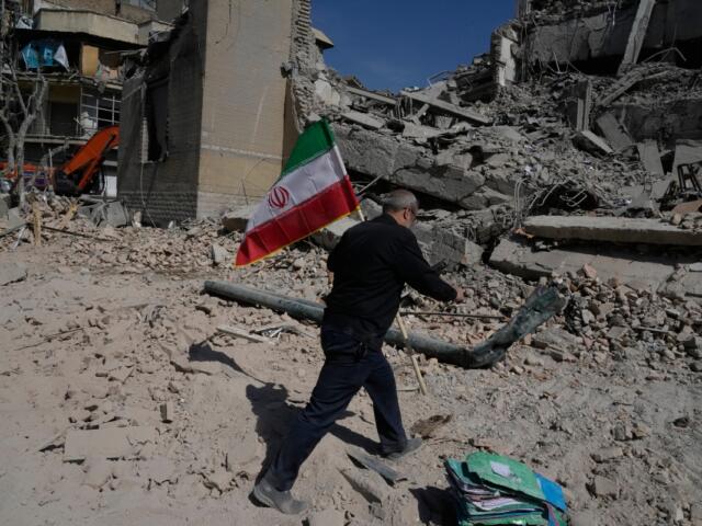 A man carries an Iranian flag to place on the rubble of a police facility struck during the U.S.–Israeli military campaign in Tehran, Iran, Wednesday, March 4, 2026. (AP Photo/Vahid Salemi)