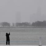 A person bundles up and fishes on a breakwater by Montrose Harbor, Monday morning, March 16, 2026, in downtown Chicago. (AP Photo/Kiichiro Sato)