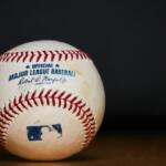 Official Major League Baseball with blue logo and red seams on a dark background.