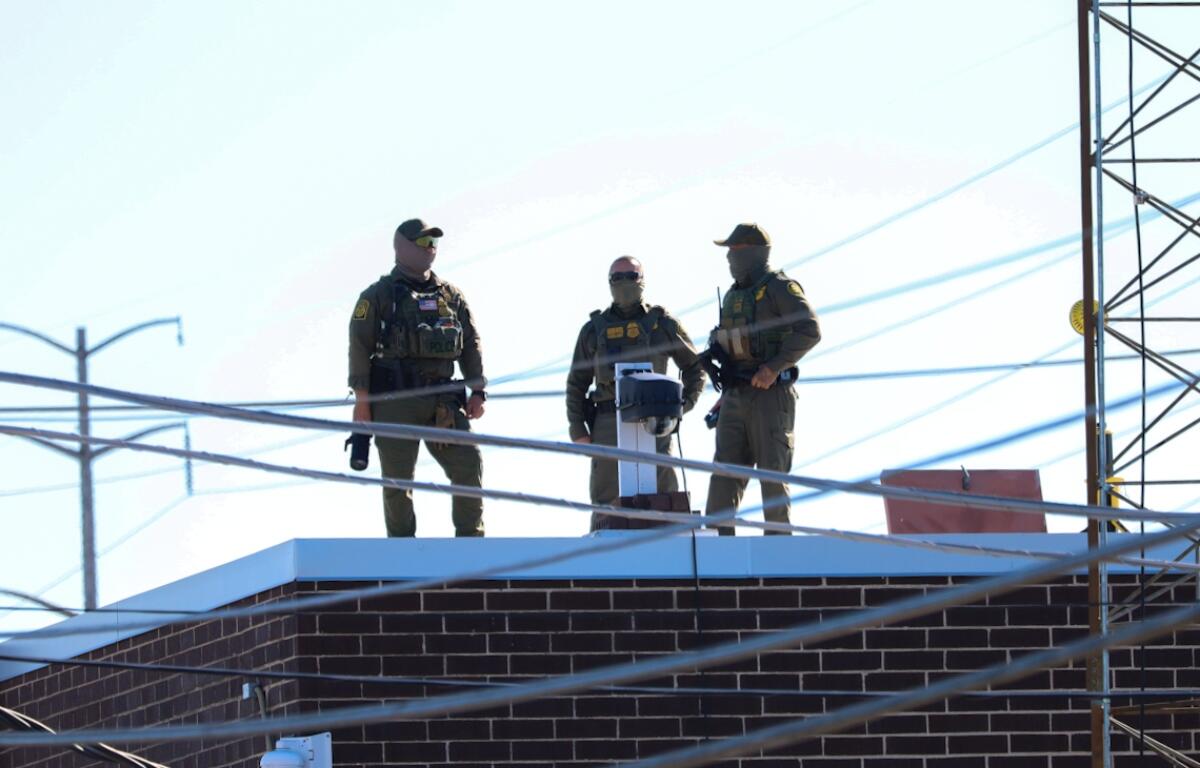 Three men in Customs and Border Protection uniforms stand on the roof of a Broadview immigration facility taking pictures of the surrounding area on Oct. 9, 2025. (Capitol News Illinois photo by Andrew Adams)
