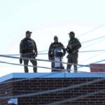 Three men in Customs and Border Protection uniforms stand on the roof of a Broadview immigration facility taking pictures of the surrounding area on Oct. 9, 2025. (Capitol News Illinois photo by Andrew Adams)