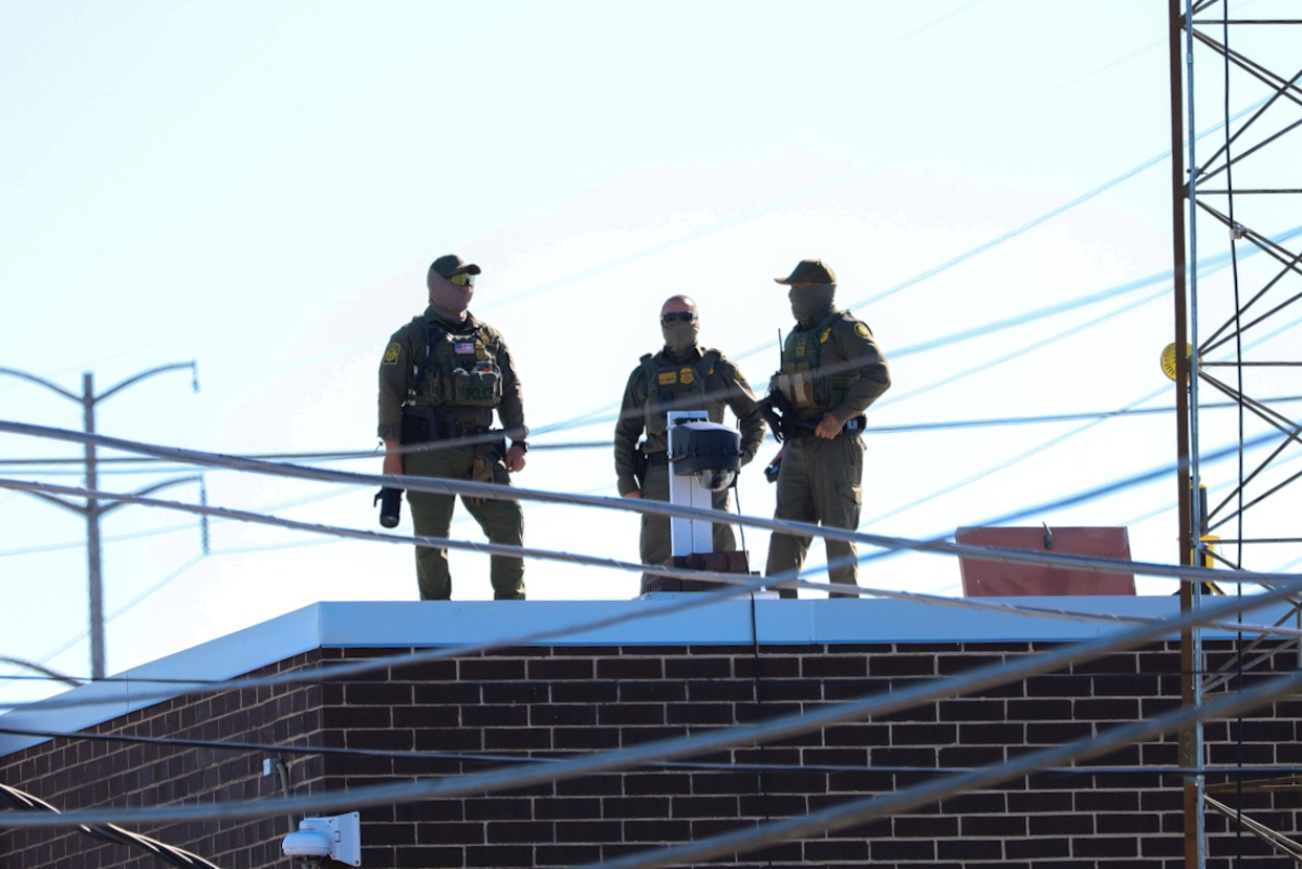 Three men in Customs and Border Protection uniforms stand on the roof of a Broadview immigration facility taking pictures of the surrounding area on Oct. 9, 2025. (Capitol News Illinois photo by Andrew Adams)