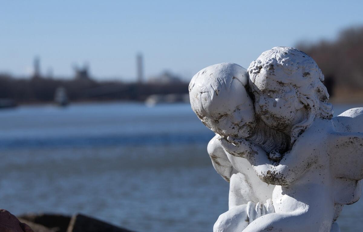 A statue of two angels showing the consequences of air pollution is seen with their backs to the Illinois river and the Powerton coal plant. (Medill Illinois News Bureau photo by Gabriel Castilho)