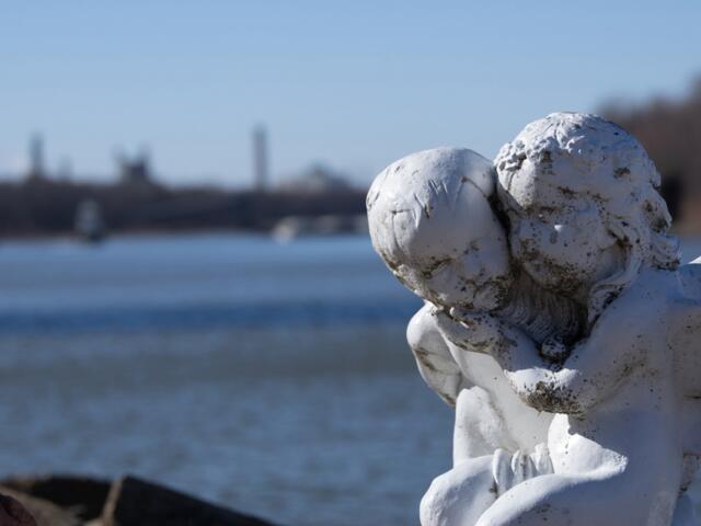 A statue of two angels showing the consequences of air pollution is seen with their backs to the Illinois river and the Powerton coal plant. (Medill Illinois News Bureau photo by Gabriel Castilho)