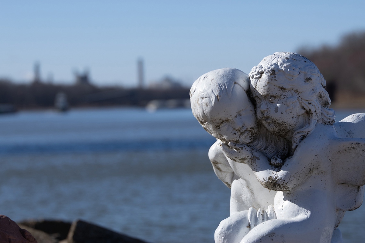 A statue of two angels showing the consequences of air pollution is seen with their backs to the Illinois river and the Powerton coal plant. (Medill Illinois News Bureau photo by Gabriel Castilho)