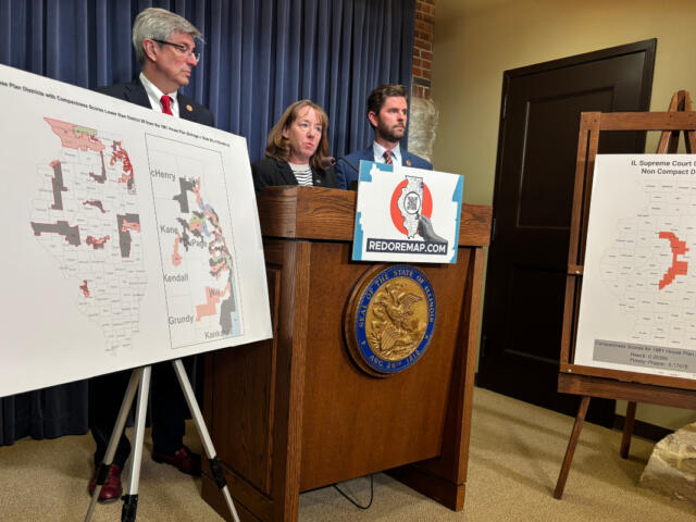 Three people stand behind a wooden podium with a REDOREMAP.COM sign, flanked by large district maps on easels.