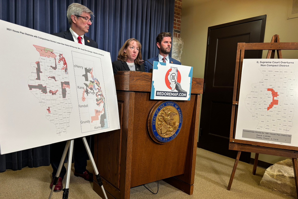 Three people stand behind a wooden podium with a REDOREMAP.COM sign, flanked by large district maps on easels.