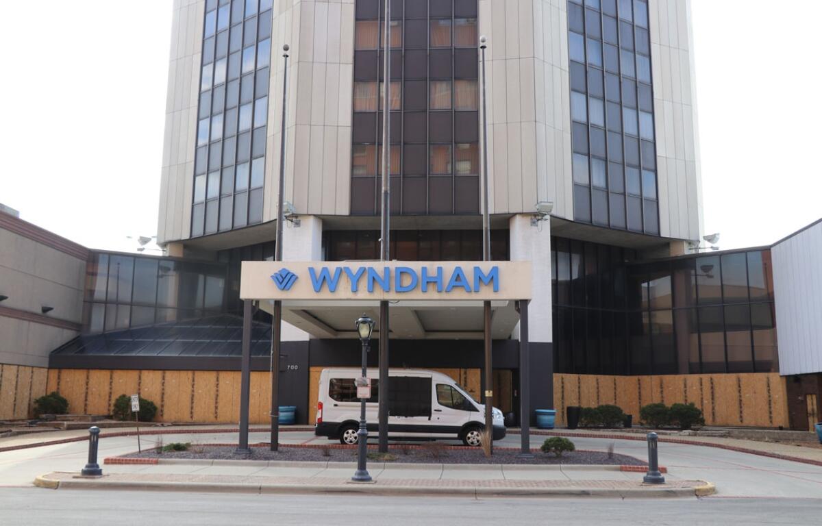 Front entrance of a multi-story Wyndham hotel with a white van parked under the porte-cochère and a blue Wyndham sign above the doorway