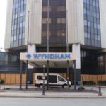 Front entrance of a multi-story Wyndham hotel with a white van parked under the porte-cochère and a blue Wyndham sign above the doorway